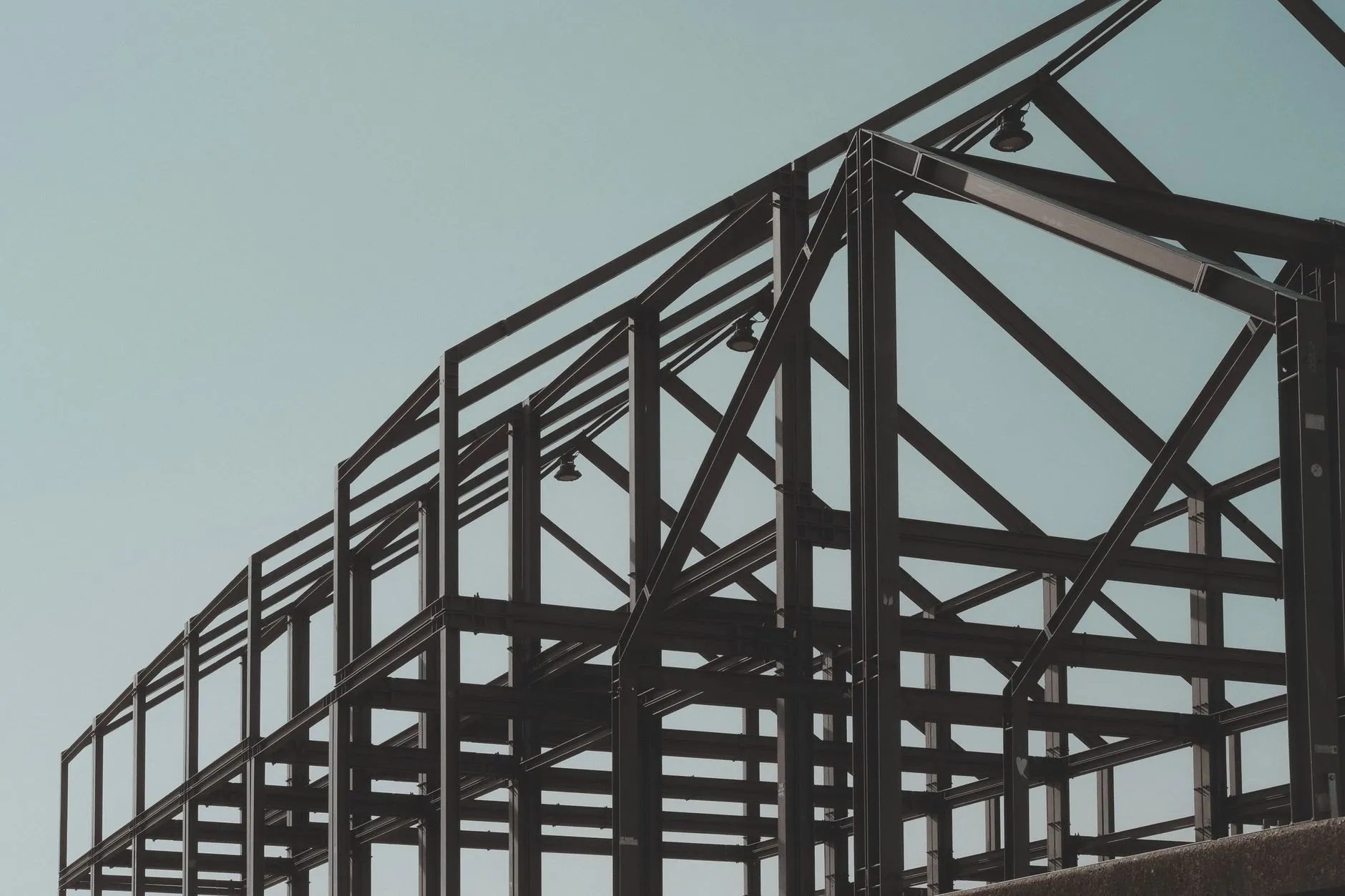 A dark steel frame of beams and bracing against a pale sky