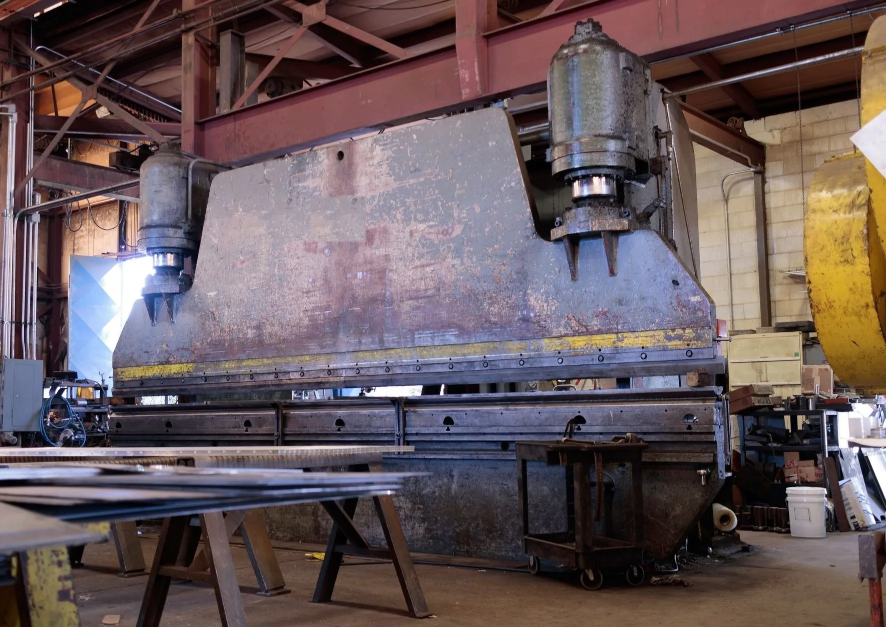 A heavy press brake standing in the fabrication shop with sheet stacked on trestles in front