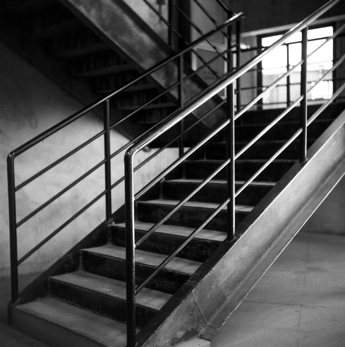 A black steel stair with a bar handrail rising towards a bright window