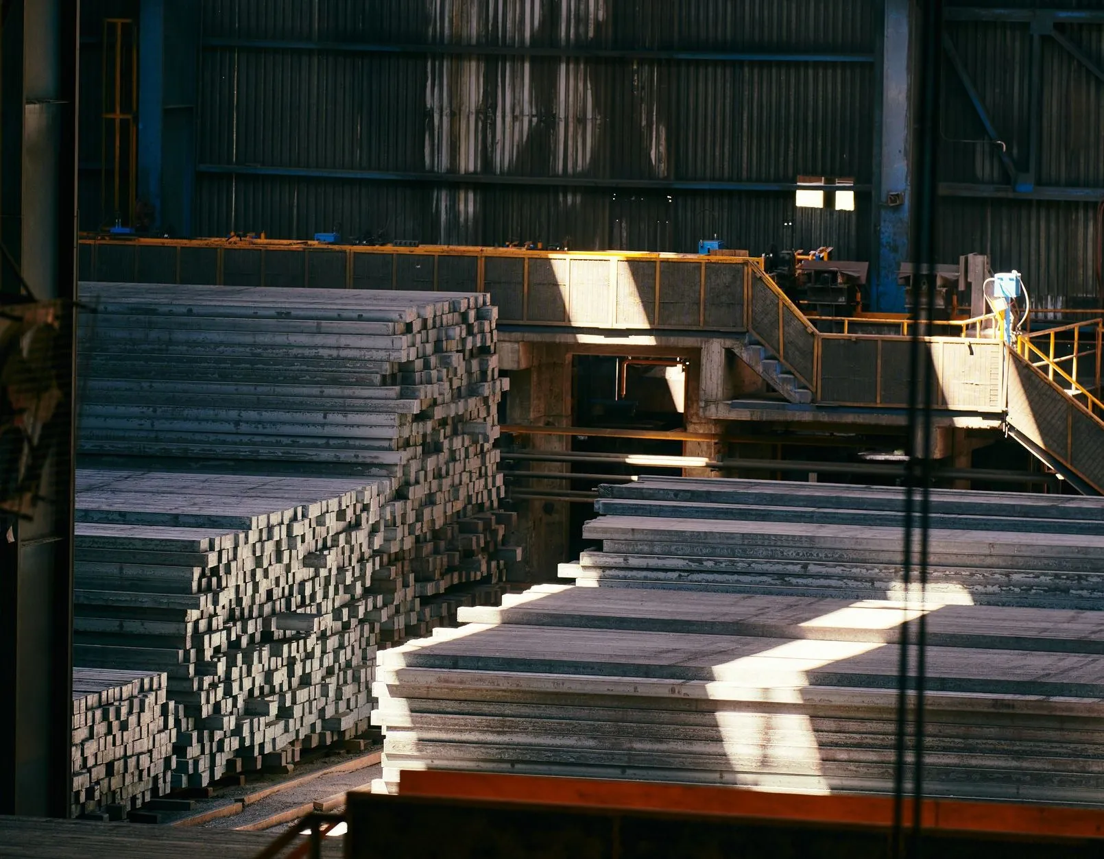 Stacks of steel bar and plate in the stockholding bay under shafts of light